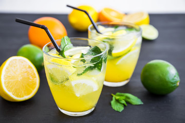Refreshing citrus lemonade with limes and lemons in glasses on dark table