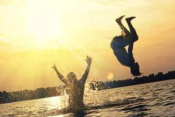 Glückliche junge Menschen laufen und springen am See beim Sonnenuntergang