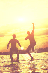 Fototapeta premium Glückliche junge Menschen laufen und springen am See beim Sonnenuntergang