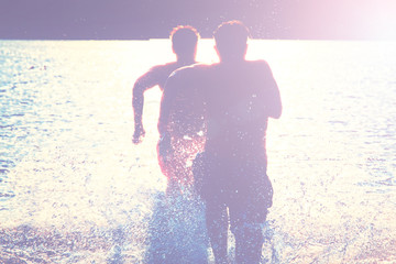 Glückliche junge Menschen laufen und springen am See beim Sonnenuntergang