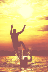 Fototapeta na wymiar Glückliche junge Menschen laufen und springen am See beim Sonnenuntergang