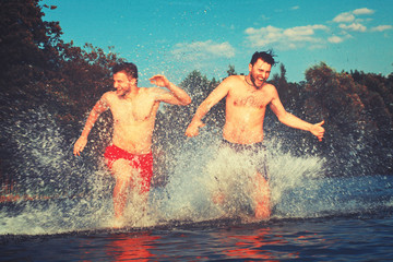 Glückliche junge Menschen laufen und springen am See beim Sonnenuntergang