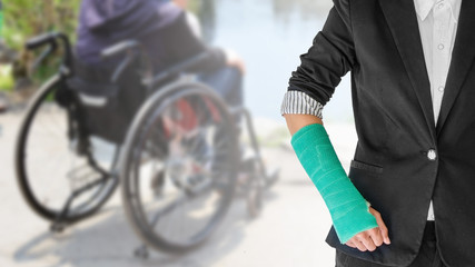 Obraz premium Female patient wearing black suit with green cast on arm isolated on blurred background patient sitting on wheelchair, body injury concept