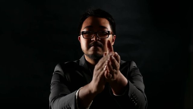 Serious Businessman in Black Suit clap hands for good job on black wall background.