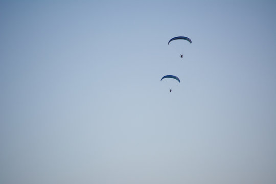Silhouette of a male paraglider on a paraplan against a background of a sunset in the sky and clouds hovering over the sea. Concept: freedom, loneliness, hobby, sport.