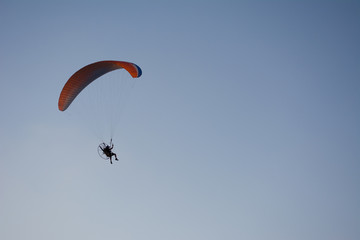 Silhouette of a male paraglider on a paraplan against a background of a sunset in the sky and clouds hovering over the sea. Concept: freedom, loneliness, hobby, sport.