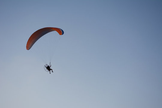Silhouette of a male paraglider on a paraplan against a background of a sunset in the sky and clouds hovering over the sea. Concept: freedom, loneliness, hobby, sport.
