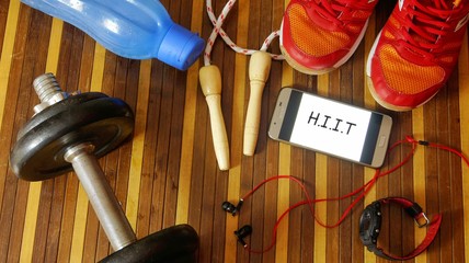 Fitness, healthy and active lifestyles concept. Dumbbells, sport shoes, smart phone with earphone, skipping rope and water bottle gym floor with word H.I.I.T (high intensity interval training)