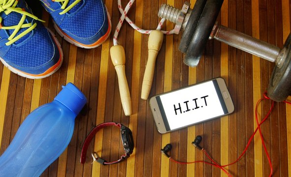 Fitness, healthy and active lifestyles concept. Dumbbells, sport shoes, smart phone with earphone, skipping rope and water bottle gym floor with word H.I.I.T (high intensity interval training)