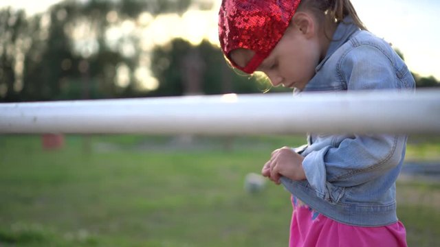 Little girl in a stylish baseball cap trying to button up her jute jaket at sunset