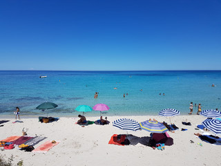 La Plage de Ghjunchitu &agrave; Corbara (Haute-Corse). Du sable blanc et des nuances de couleur bleue. Quelques parasols, serviettes et des baigneurs dans l&rsquo;eau. Une belle vue sur l&rsquo;horizon.