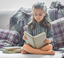 little girl reading book on sofa