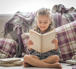 little girl reading book on sofa