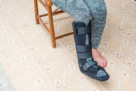 woman with black cast on leg sitting on wood chair, body injury concept