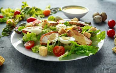 Fresh healthy Caesar salad with chicken, egg quail, tomatoes, Cheese and Croutons in a white plate