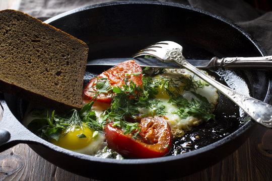 Eggs fried tomatoes in a cast-iron frying pan Wooden vintage background
