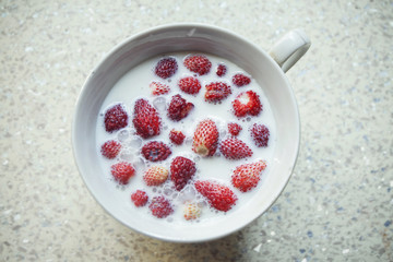Strawberries in milk, in a white cup. On a beige table