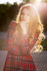 Pretty blonde model in fashionable checkered dress posing in rays of sun