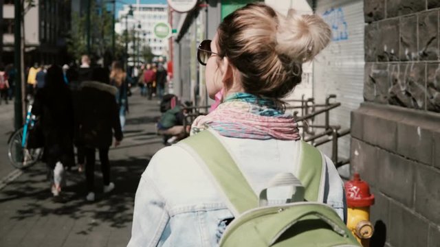 Young beautiful woman with backpack walking in the urban city and taking photos, using the smartphone for this.