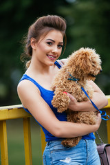 Portrait of beautiful smiling young woman standing on bridge with her little red poodle puppy. 
