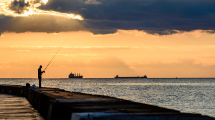 Fototapeta premium people enjoying sunset on the breakwater in the sea with lighthouse