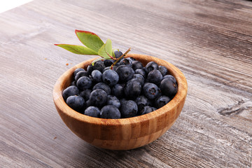 Freshly picked blueberries in wooden bowl. Juicy and fresh blueberries with green leaves on rustic table. Bilberry on wooden Background. Blueberry antioxidant. Concept for healthy eating and nutrition