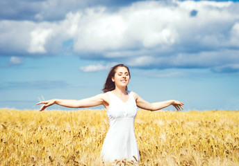 Beautiful and happy girl in a white dress walking in a meadow at summer.