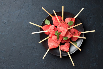 Watermelon heart shaped popsicles in black plate on dark blue stone background.