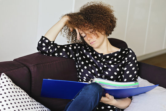 jeune et jolie femme rousse &eacute;tudiant ses cours dans un divan &agrave; la maison