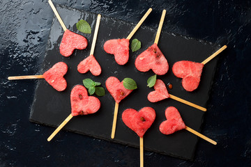 Fototapeta na wymiar Watermelon heart popsicles with mint on black slate board.