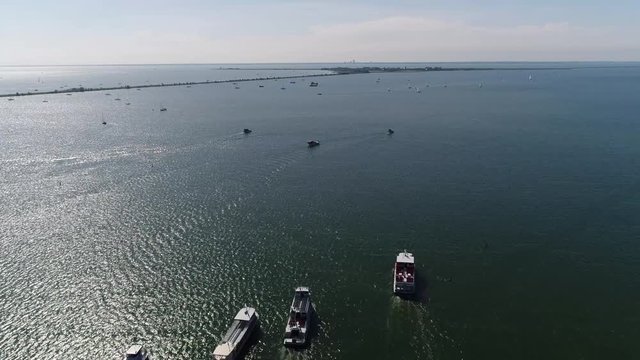 Aerial over Markermeer showing Marken in background flying forwards over squadron of tourist boats sailing in formation next to eachother towards Marken bird-eye view stable flight beautiful day 4k