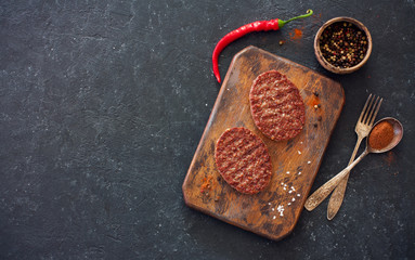 Two beefsteaks , peppers and old spoon, fork and cutting board over black stone background