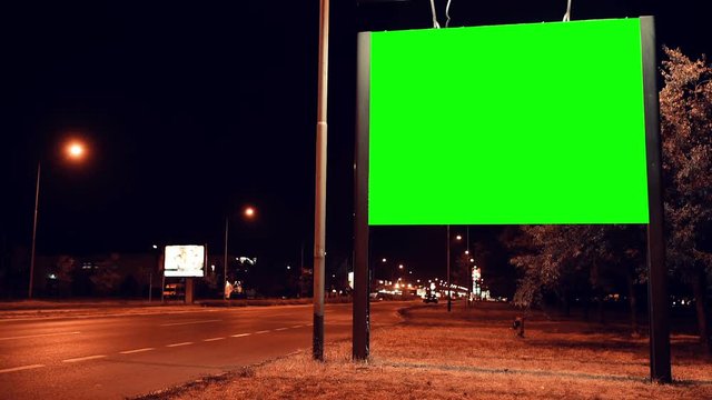 Blank green screen advertising billboard on street at night with traffic time lapse, useful for chroma keying