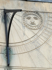 old sundial in close up with roman numeral and a carved symbol of the sun
