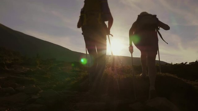 Silhouettes of tourists climbing a mountain in the rays of the setting sun. Back view. Concept - leadership and achievements