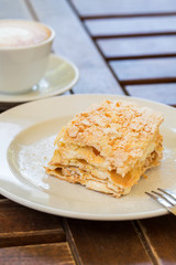 Napoleon cake, cappuccino coffee on a wooden table on the veranda in the cafe, in the garden