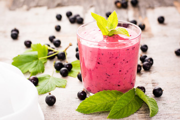Smoothies with black currant and yogurt and mint leaves. Transparent glass standing on a wooden...