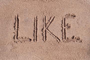 Handwritten word "LIKE" on brown sand on the beach in sunny day