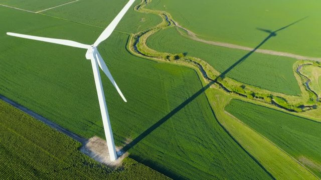 Flying through wind farm turbine blades on countryside corn field. Summer season with late afternoon light