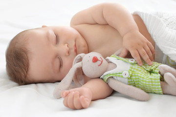 Cute little baby with toy sleeping on bed at home