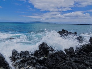 Lava Rock and Coral with Spray of crashing waves in beach tide pools at Maluaka Beach and Kihei Maui with sky and clouds