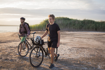 Obraz premium Two tourists with bicycle walking in the desert during the sunset in lake 