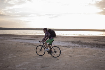 Bicycle tourist with backpacks and helmet travel in desert on his cyclocross bicycle during the sunset  