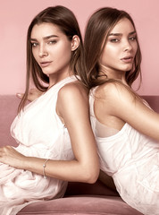 Obraz premium Fashionable twins sisters posing on pink background.