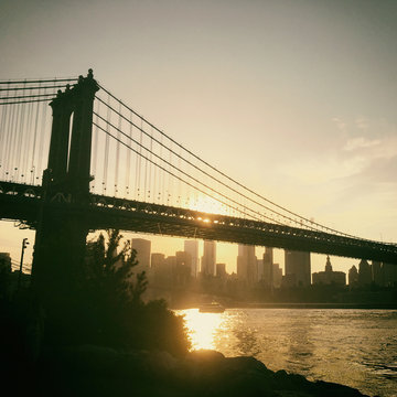 Warm light, sunset over Manhattan skyline. View of the Manhattan Bridge from Brooklyn Bridge Park looking towards Manhattan's financial district at sunset. Manhattan Bridge spanning the East River.