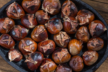 Roasted sweet chestnuts on iron pan, rustic wooden table. Autumn background. Top view