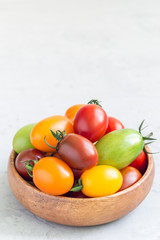 Small colorful cherry tomatoes in wooden bowl on table, vertical, copy space