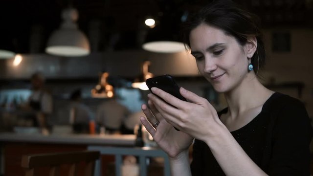 Beautiful young woman sitting in cafe and using the smartphone. Attractive female typing message on touchscreen.