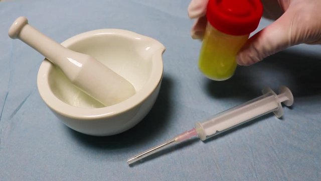 The hands  wearing rubber gloves shakes the flask with liquid and fills the syringe.