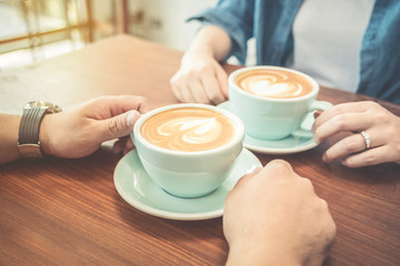hands of couple drinking coffee at cafe together ,heart shape latte art in coffee cup.